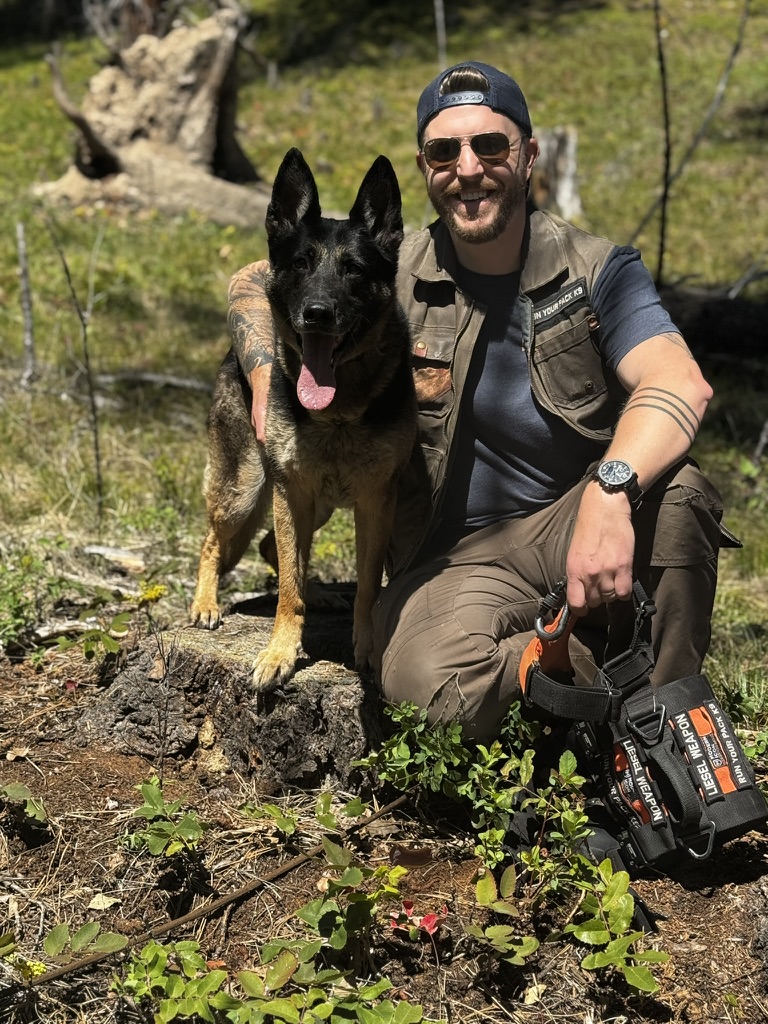 Handler kneeling with Malinois in forest